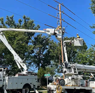 Utility workers repair power lines using bucket trucks on sunny day