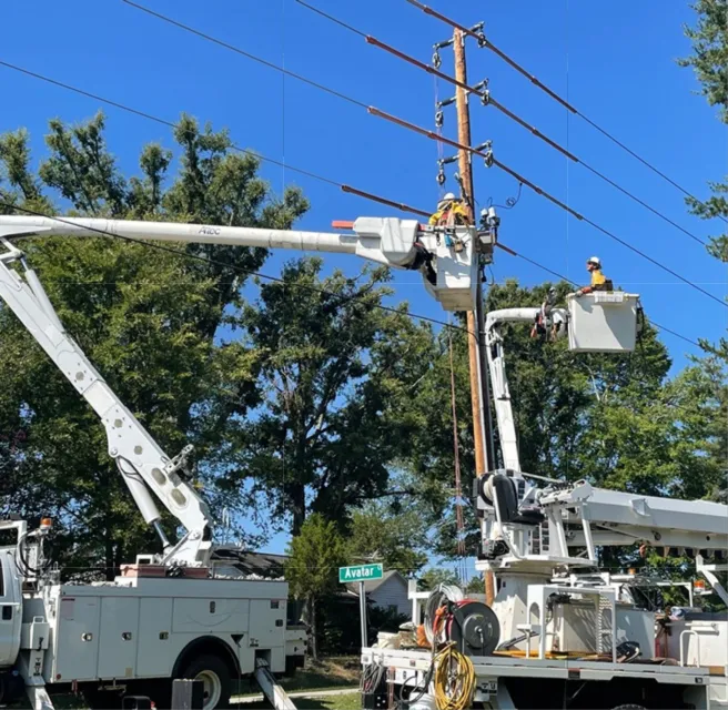 Utility workers on bucket trucks repair electrical lines on a sunny day
