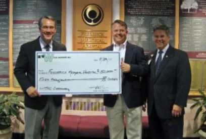 Three businessmen pose with a ceremonial donation check