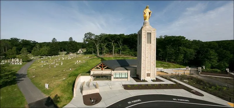 Tall golden statue memorial overlooking cemetery with trees and landscaped grounds