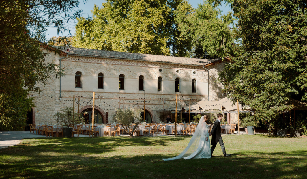 Mariés traversant les jardins d'un domaine authentique, terrasse dressée pour un week-end de mariage d'exception en France.