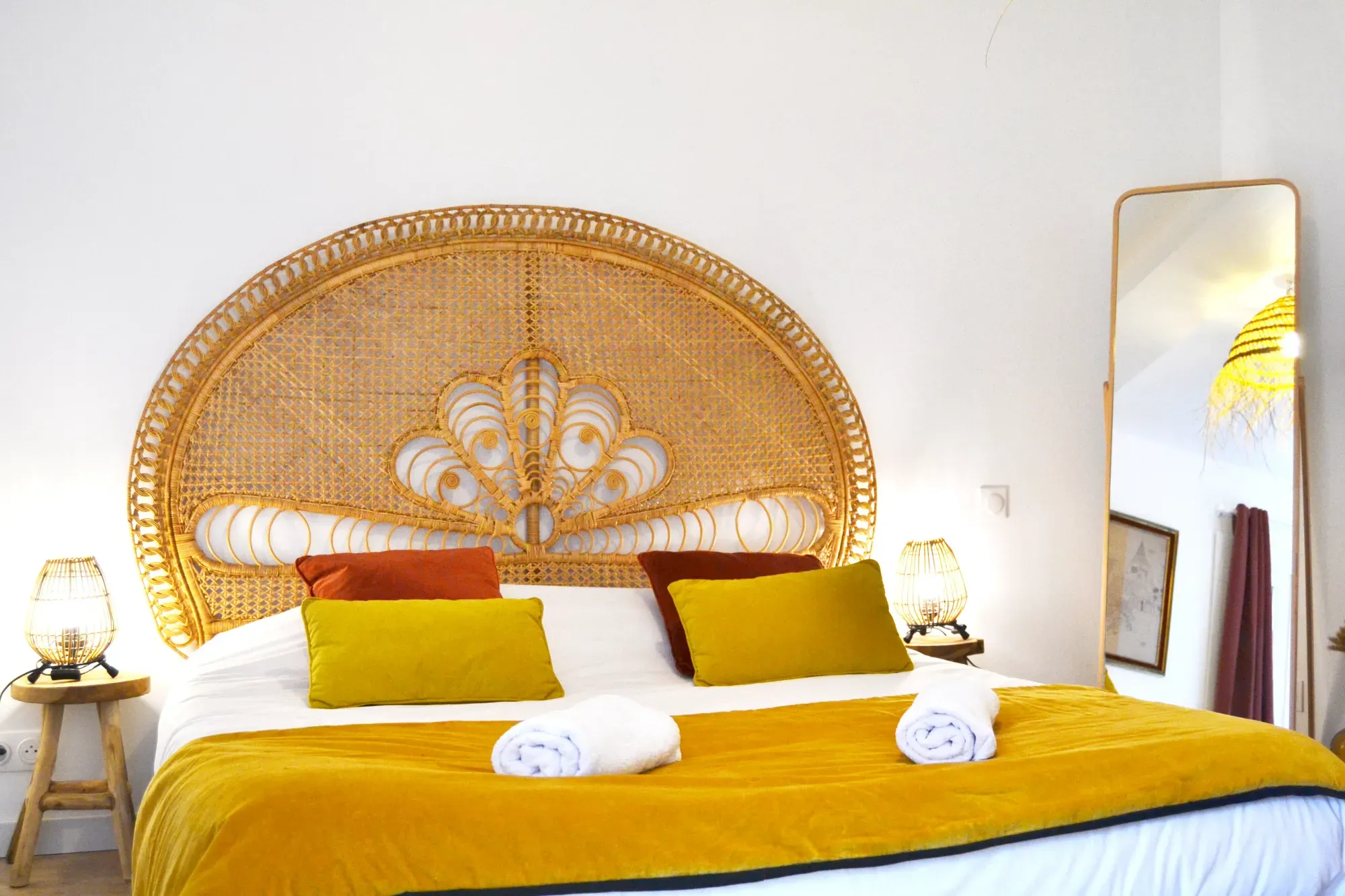 A double bed made up with clean white towels, colourful cushions and warm, atmospheric lighting in a charming bedroom.