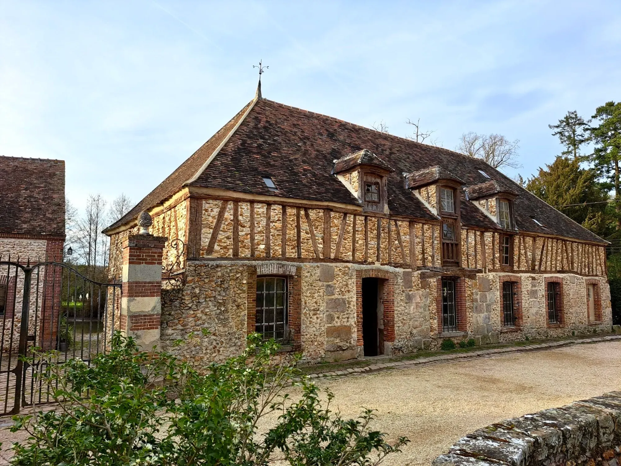 Traditional stone and timber-framed house with a brown tile roof under a clear blue sky, in a rural French architectural style.