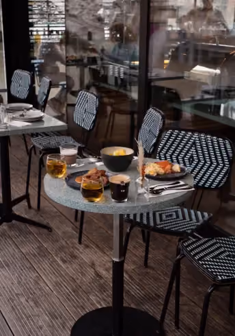 Small round table with drinks, breakfast food, and black-and-white patterned chairs on wooden floor.