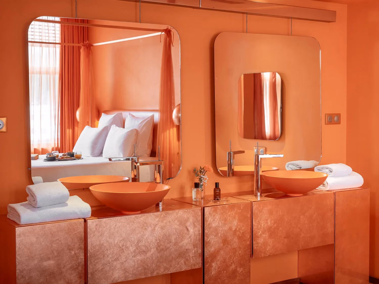Modern orange bathroom vanity with two vessel sinks, mirrors, folded towels, and small decor items.