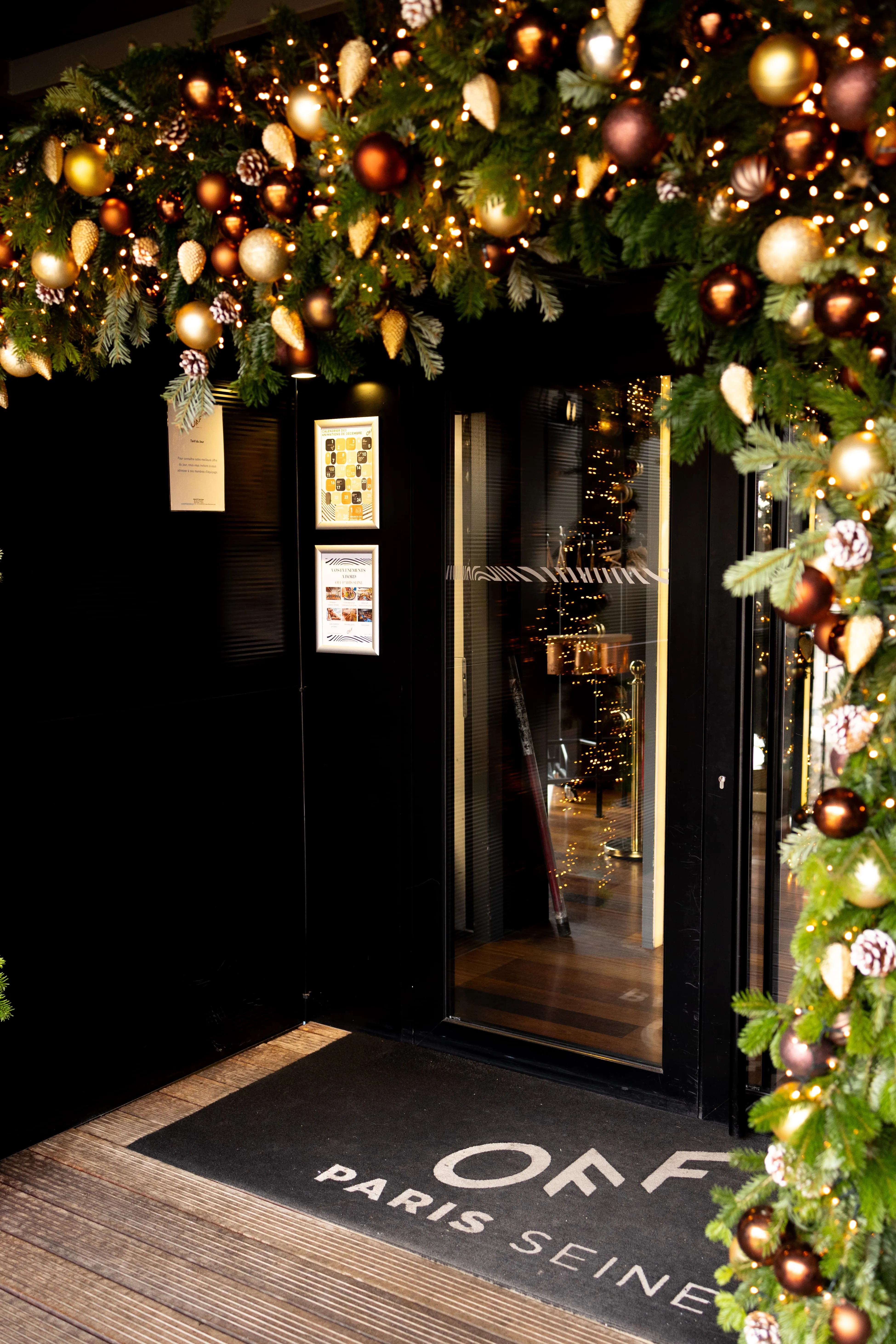 Decorated entrance with Christmas garland, lights, and a mat reading OFF Paris Seine on wooden flooring.