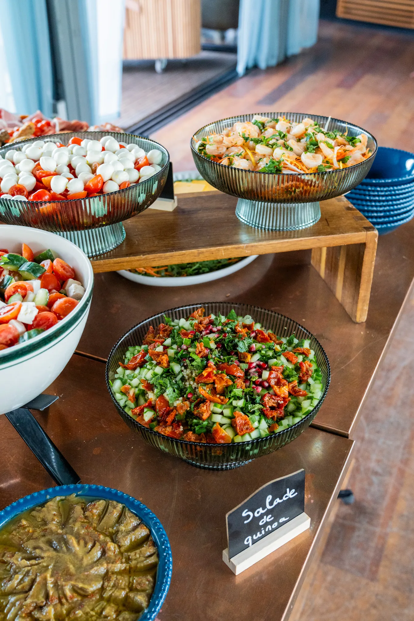 Bowls of fresh salads including quinoa salad with tomatoes, cucumber, herbs, and shrimp salad on a wooden table.