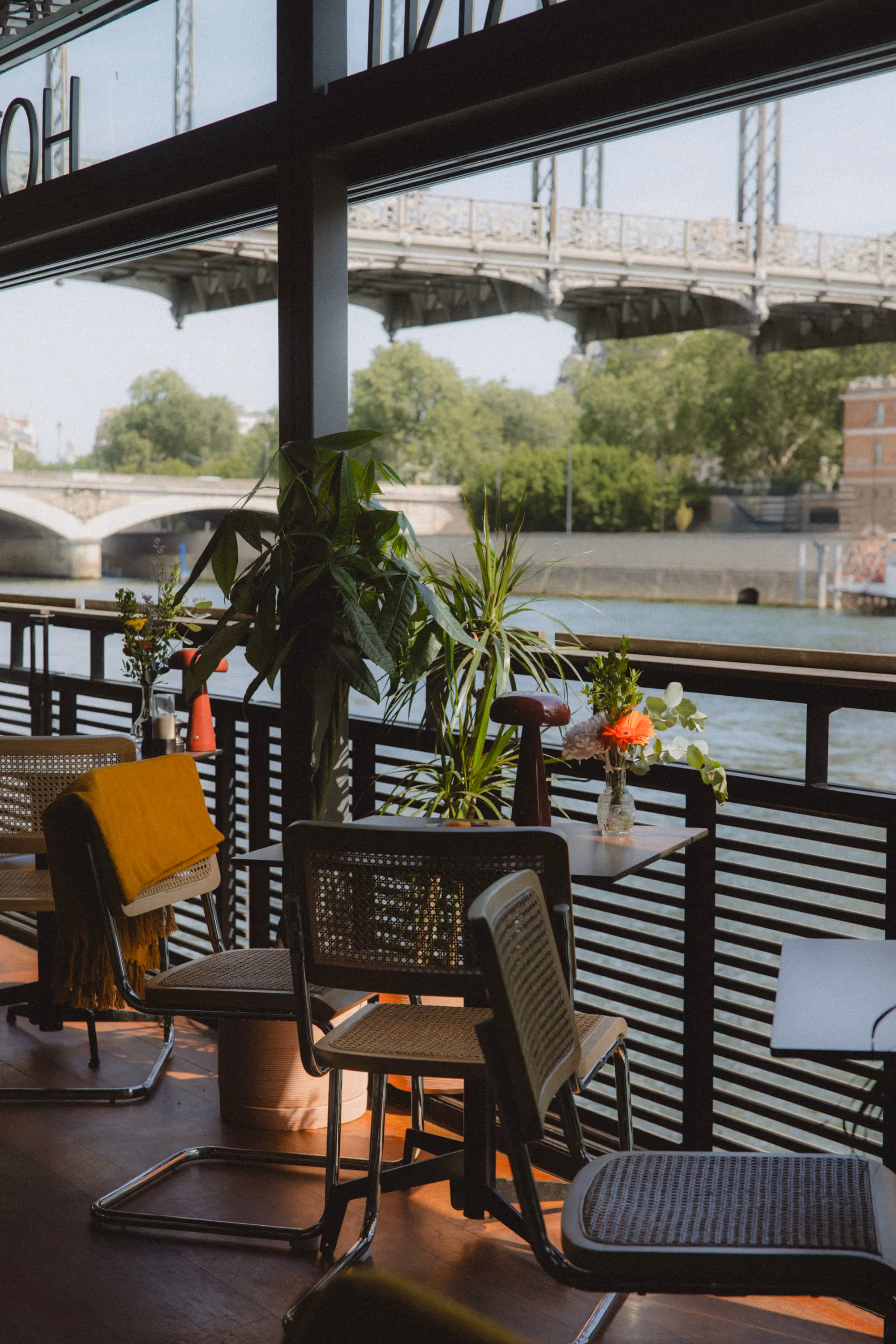 Indoor seating by window with plants and flowers overlooking a river and bridge outside.