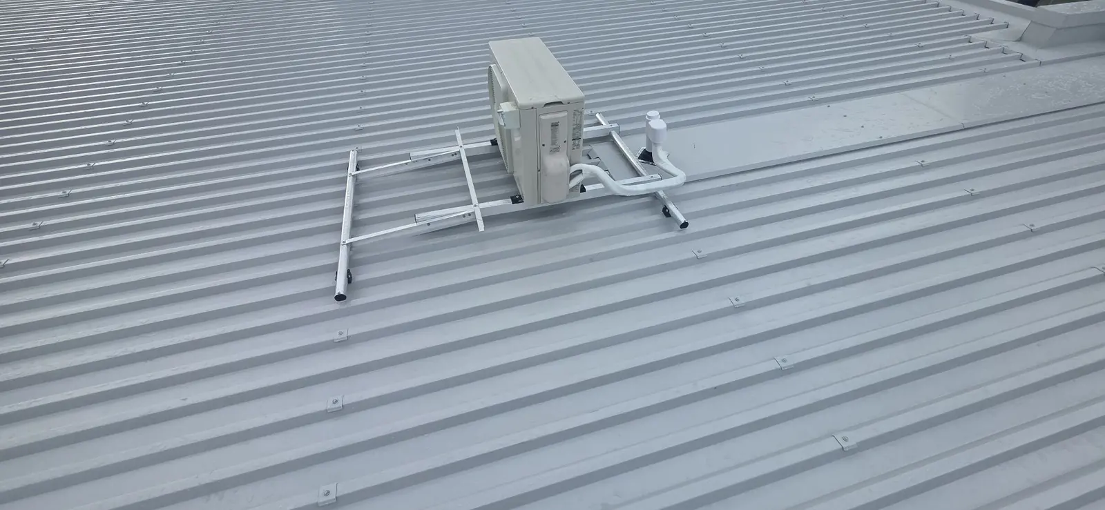 Air conditioning outdoor unit on a MonkeyToe roof bracket on a commercial roof, with its pipes running through a flashed roof penetration