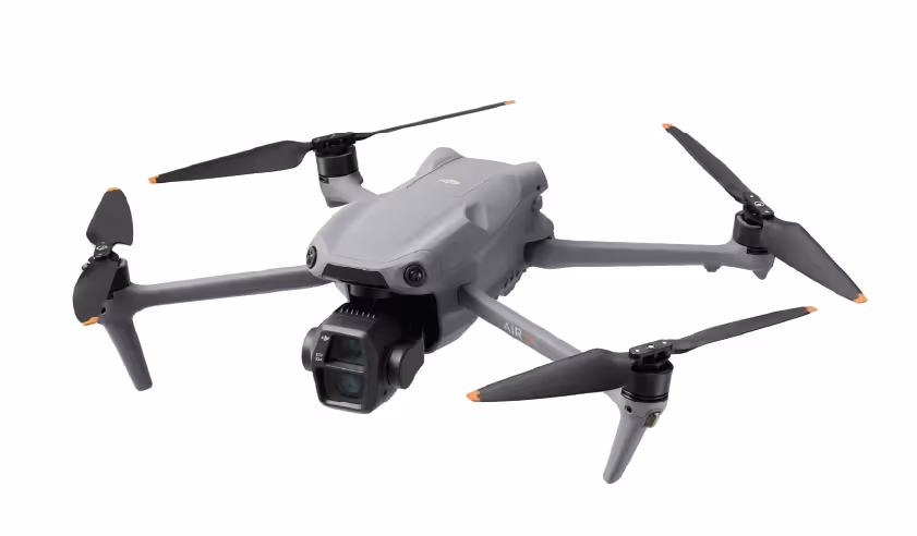 Graue Vier-Propeller-Drohne mit Kamera an der Vorderseite vor weißem Hintergrund.