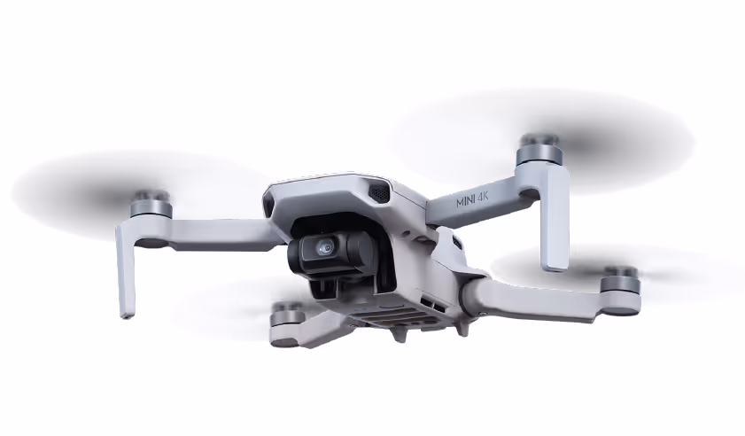 Weiße Drohne mit vier Rotoren und Kamera fliegt vor weißem Hintergrund.