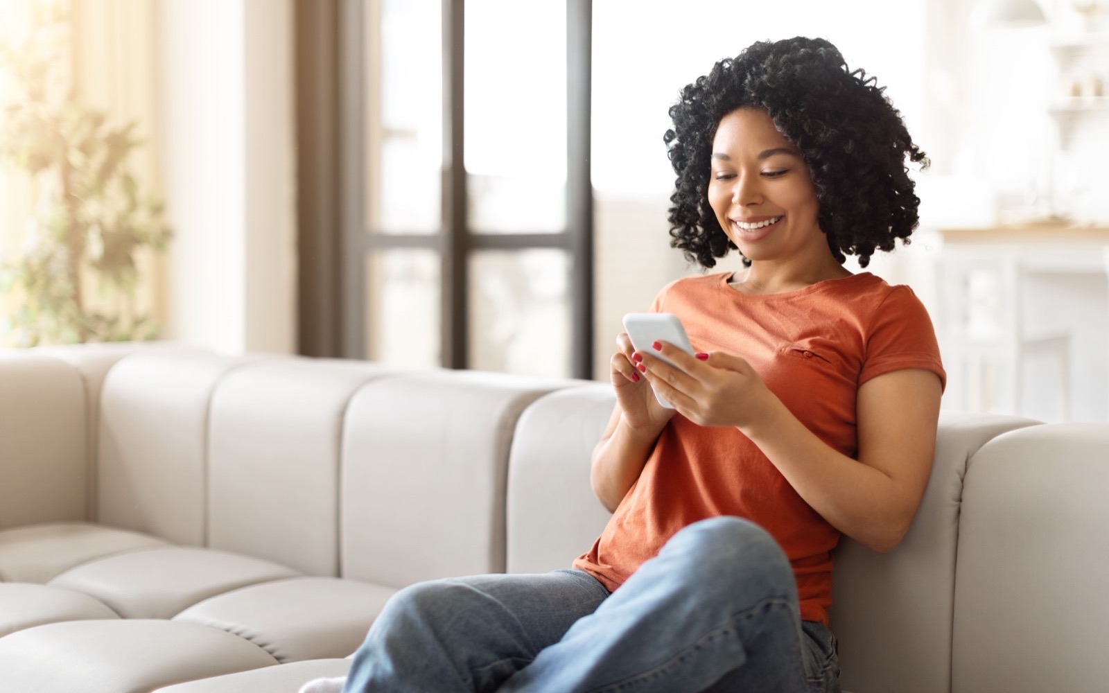 Woman smiling while using her smartphone on a sofa at home