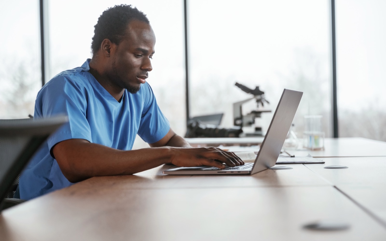 Healthcare professional in scrubs working on a laptop