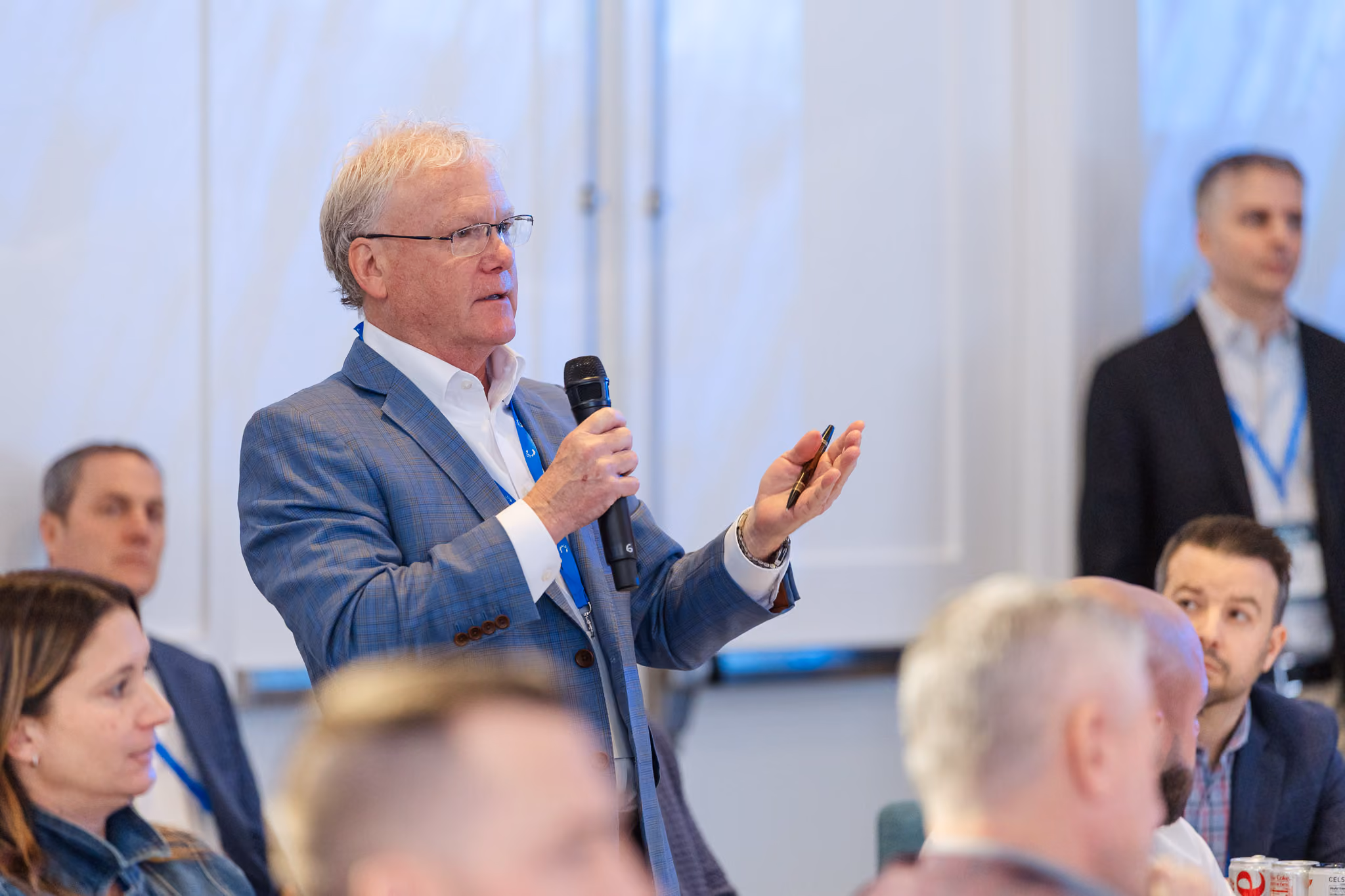 Man in a blue blazer holding a microphone speaking to an audience at a conference.