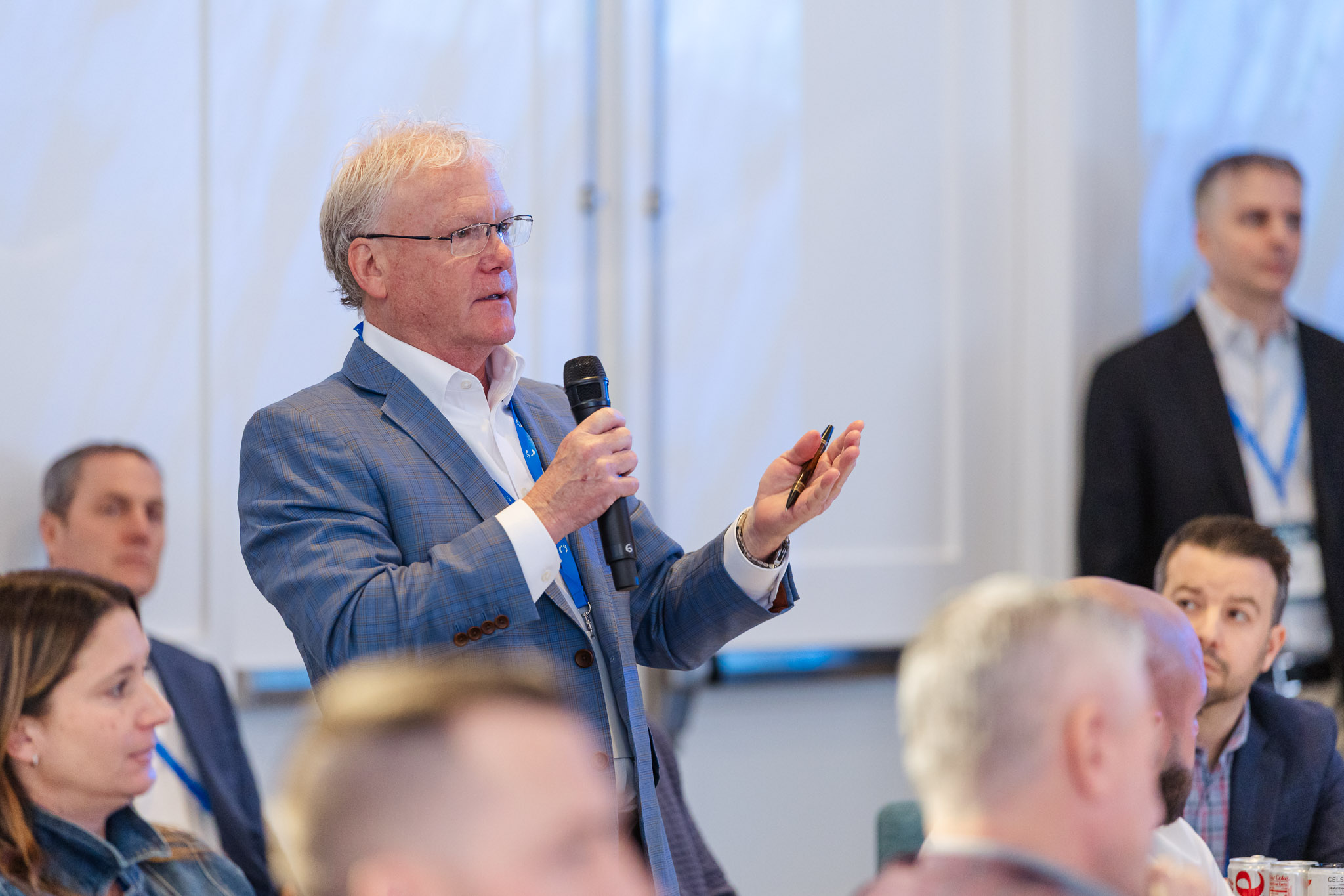 Man in a blue blazer holding a microphone speaking to an audience at a conference.