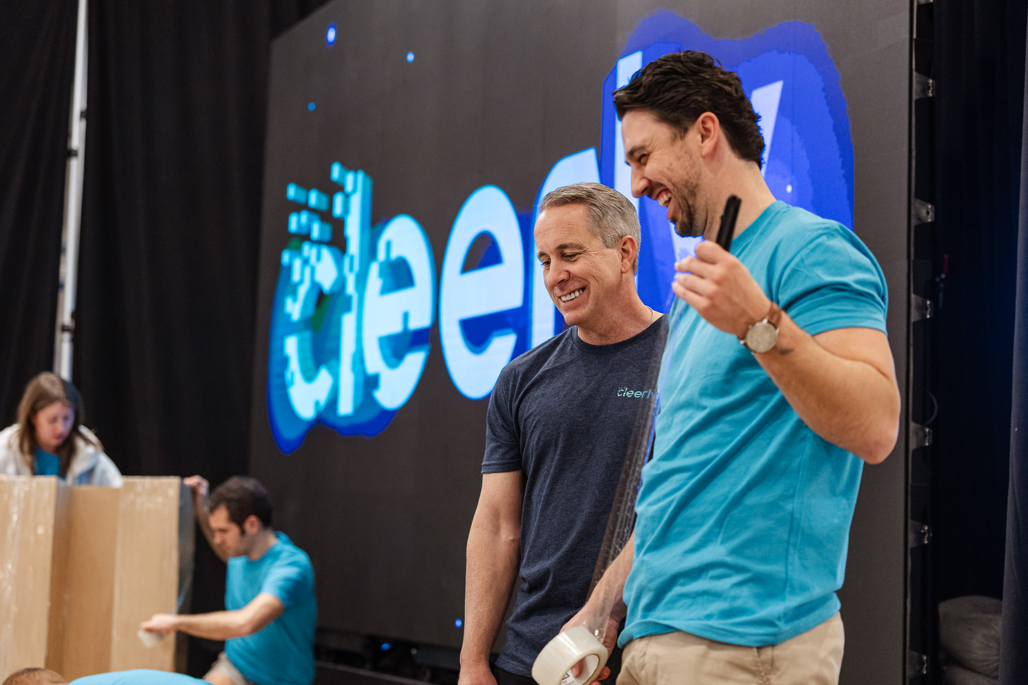 Two men smiling and talking in front of a large screen with 'cleerly' logo during setup.