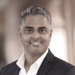 Portrait of a smiling man with short salt-and-pepper hair wearing a black suit jacket and white shirt.