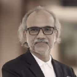 Middle-aged man with gray hair and beard wearing glasses and a black blazer over a white shirt.