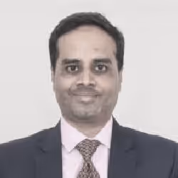Portrait of a man in a suit and tie smiling against a plain background.