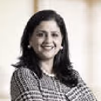 Portrait of a smiling woman with long dark hair wearing a checkered top and pearl earrings.