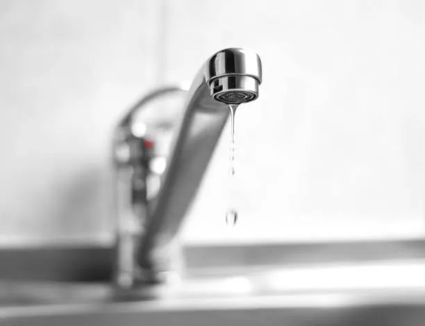 Close-up of a dripping chrome faucet with water droplets falling into a sink.
