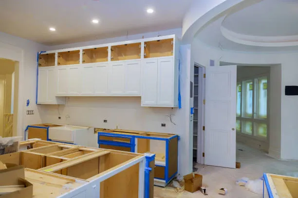 Unfinished kitchen with white cabinets partially installed and blue painter's tape on lower cabinets during renovation.