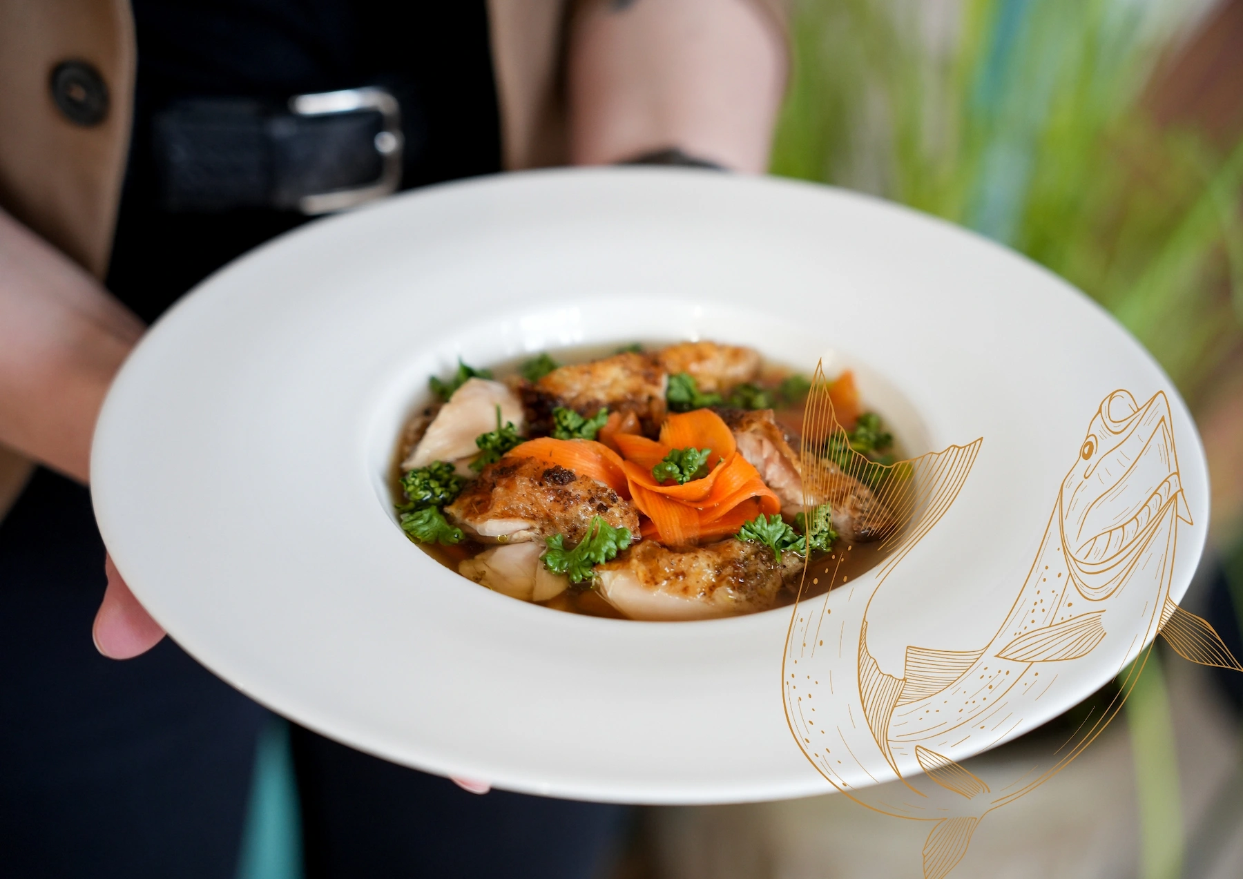 Hand holding a white plate with roasted fish fillets, garnished with carrot ribbons and fresh parsley.