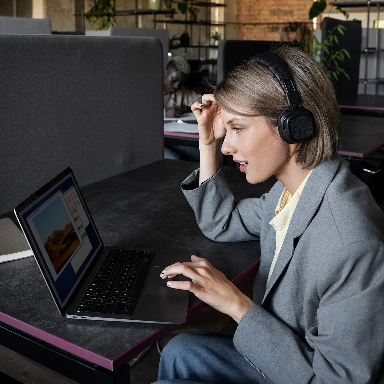 A woman sitting at a table with a laptop and headphones on.