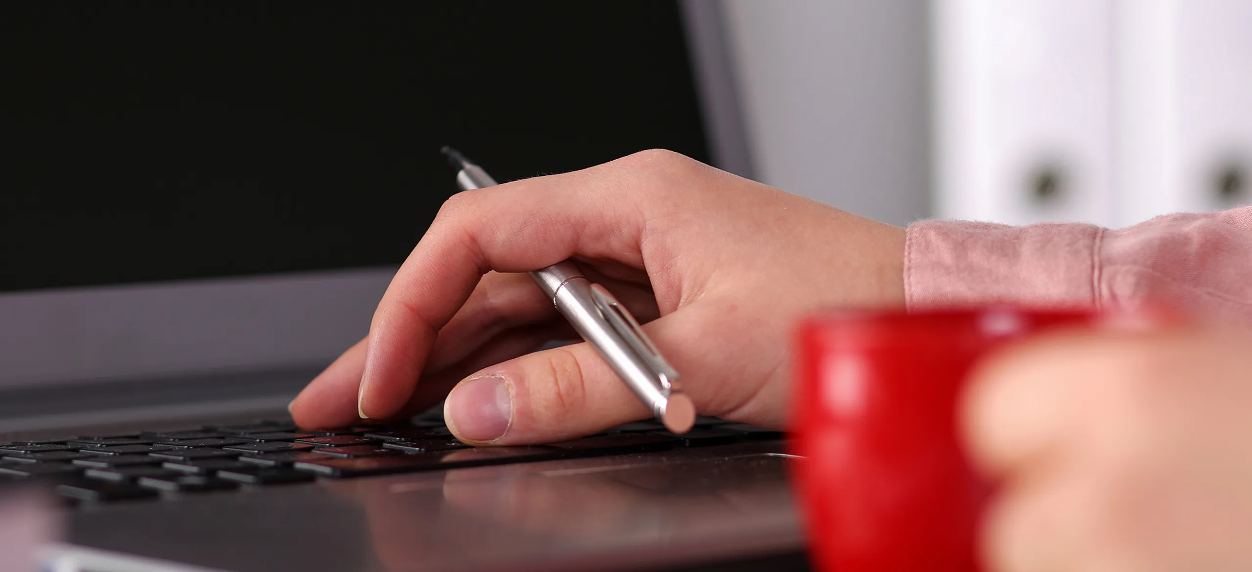 A person typing on a laptop with a pen.