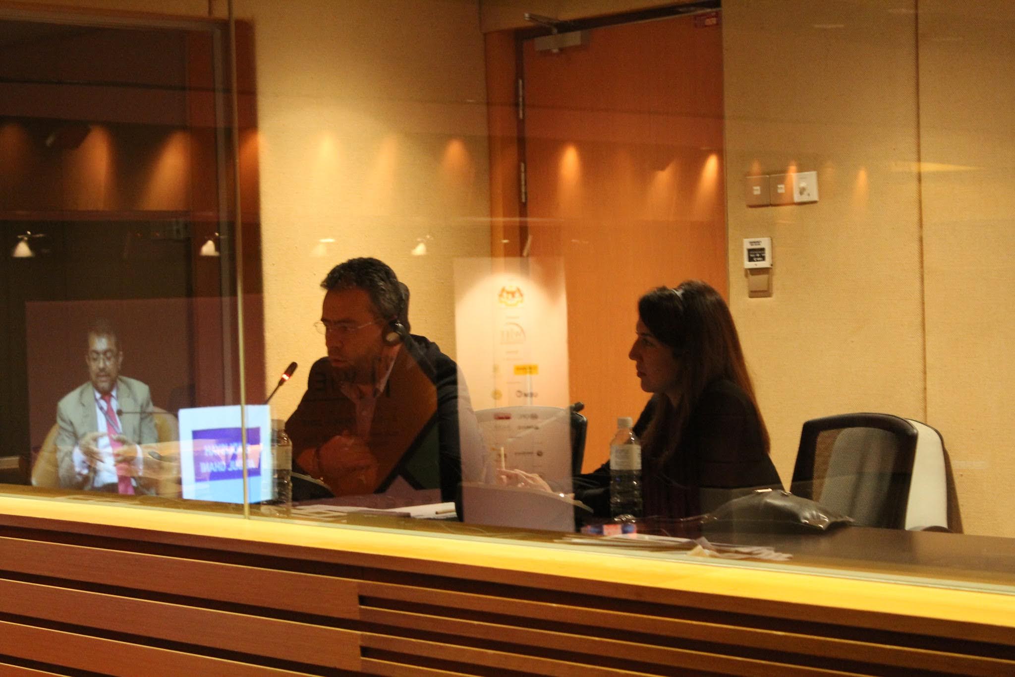 Two interpreters at work in a booth, seen through the glass