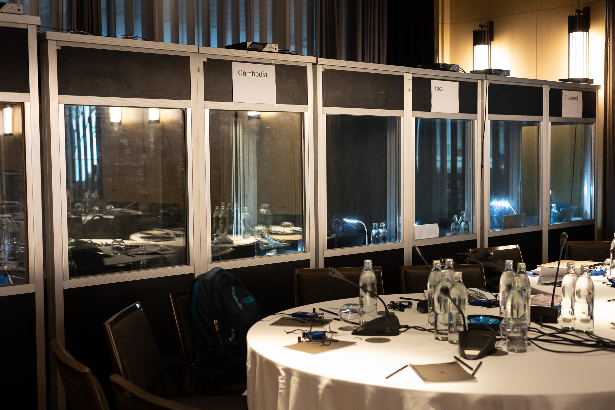 Row of interpreter booths behind a conference table set with microphones