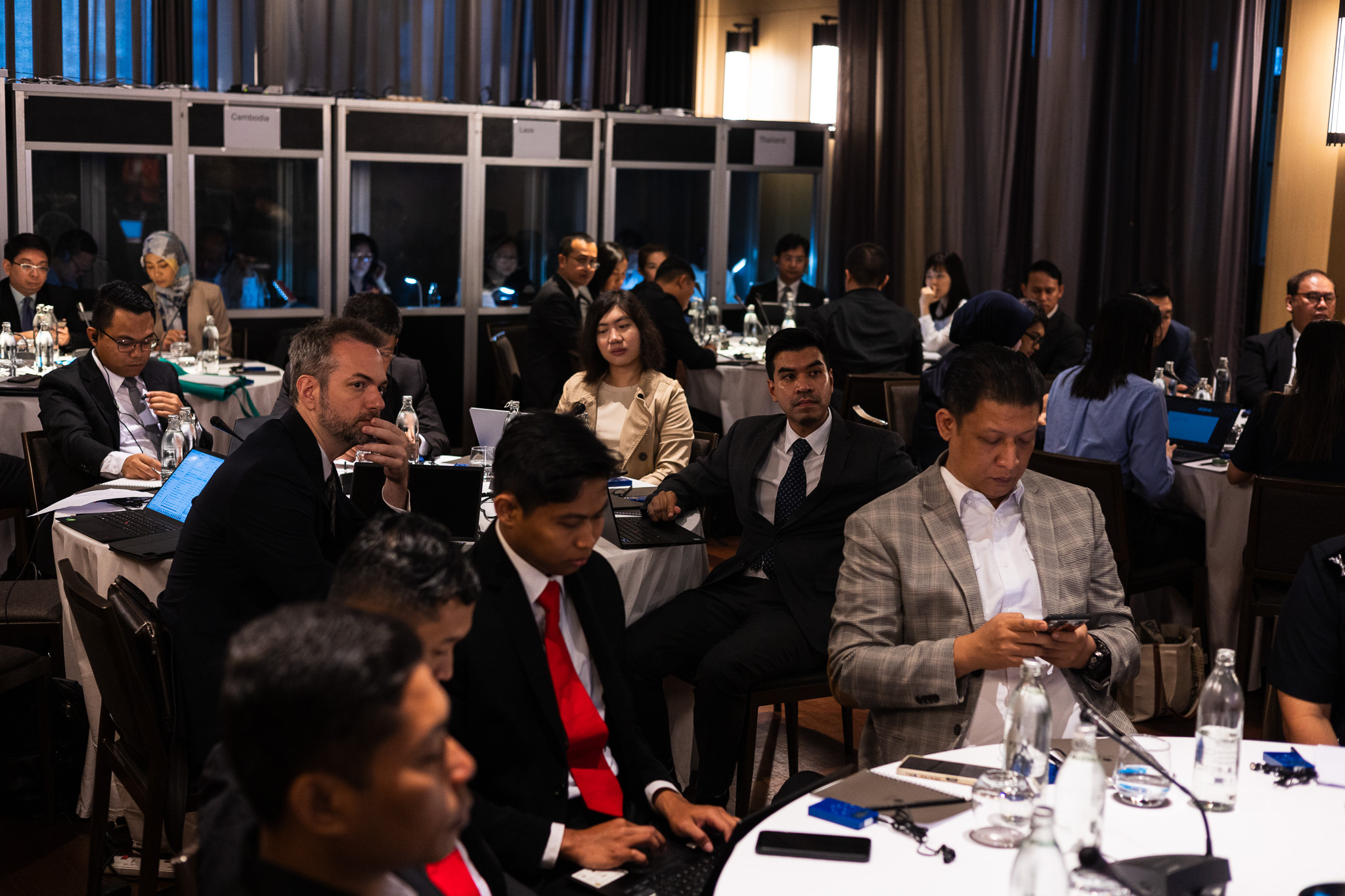 Delegates seated at round tables with interpreter booths along the back wall