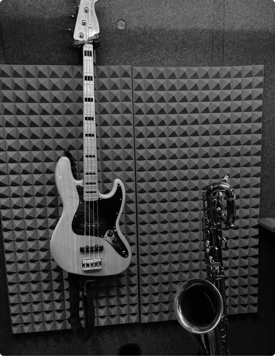 Fender Jazz bass and saxophone inside a musician's WhisperRoom soundproof rehearsal space, with acoustic studio foam on the walls.
