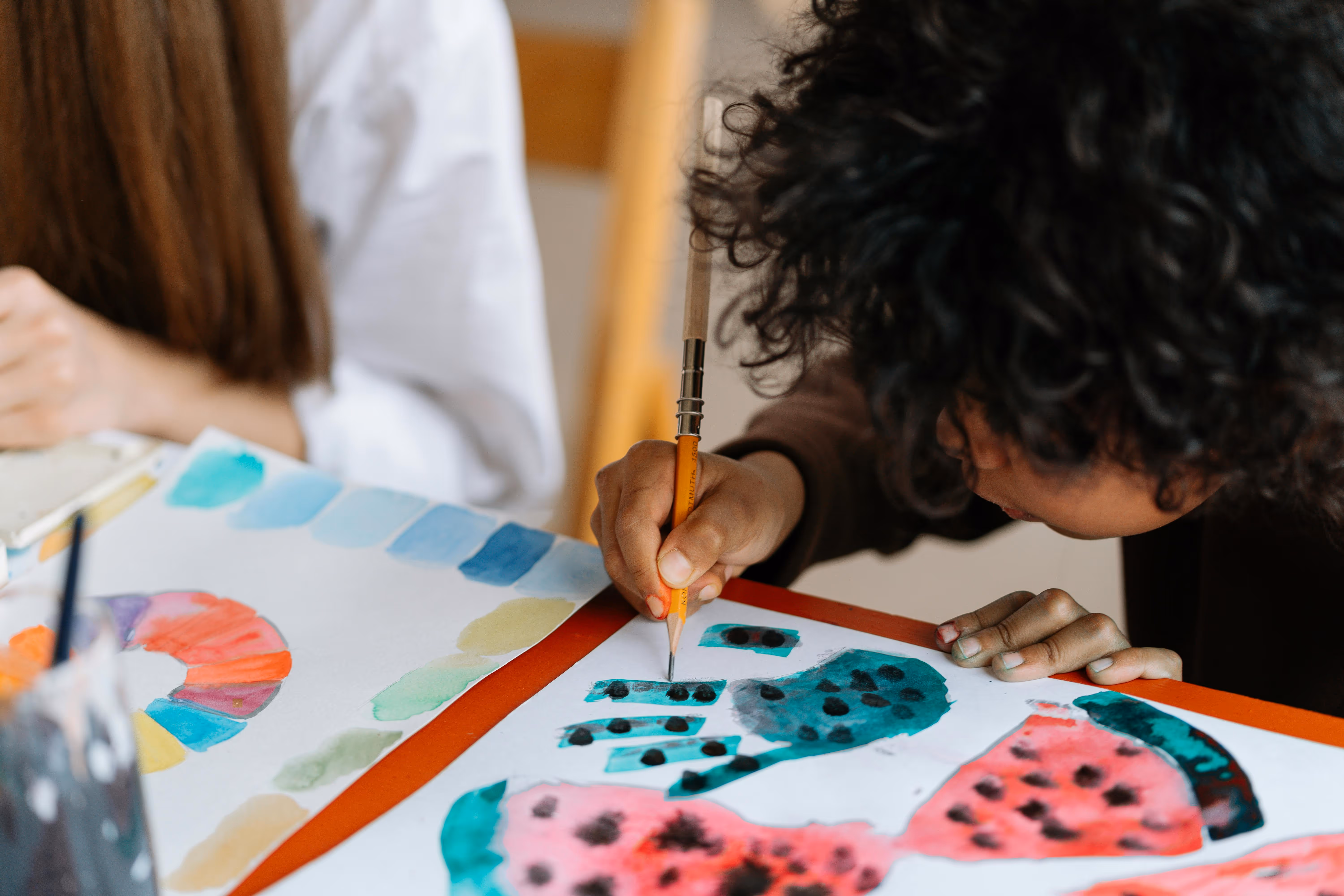A child with dark curly hair works on a watercolor painting of watermelons in a kids art class