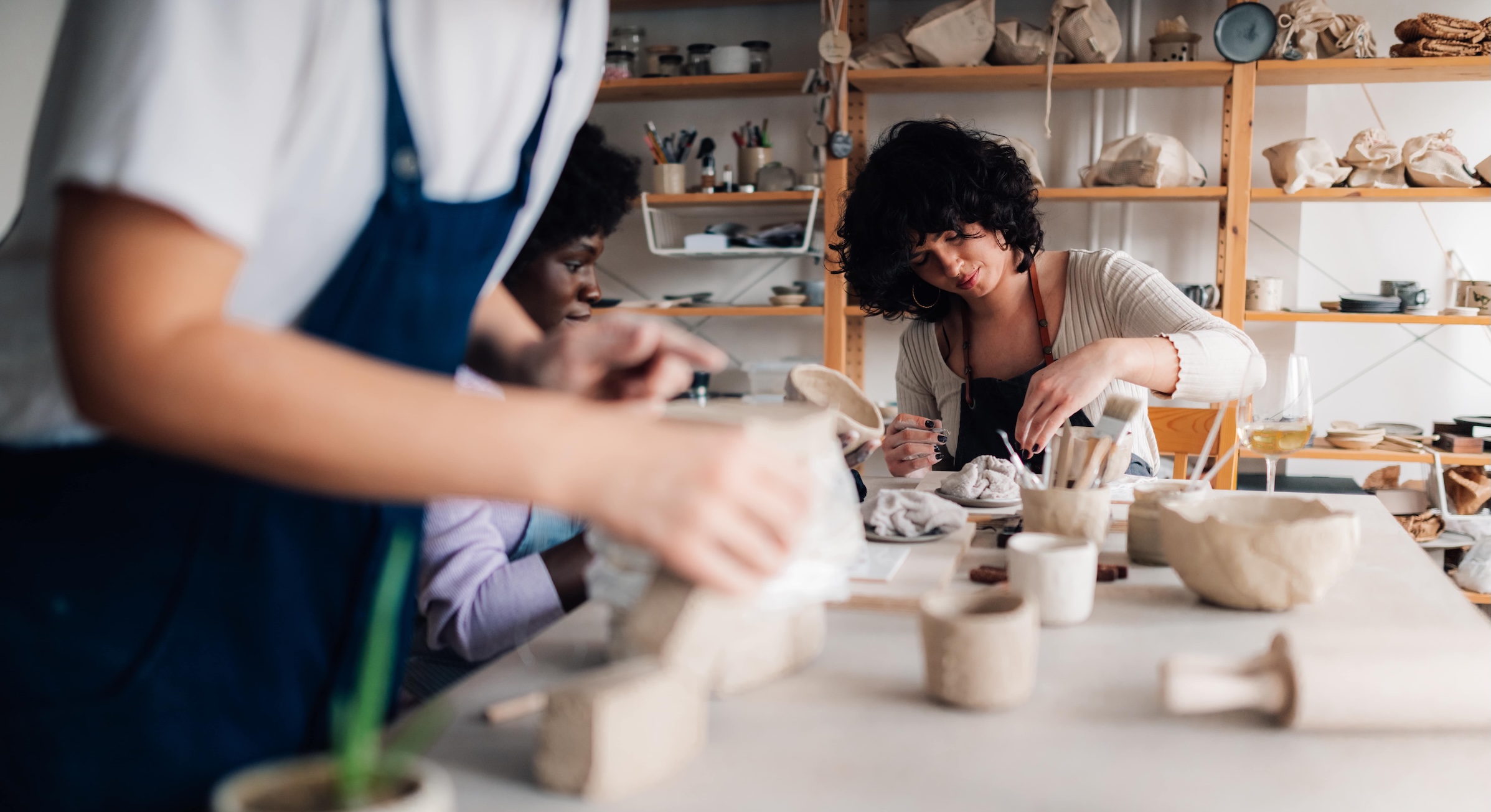 A group of students sitting at a table in a ceramics studio working on hand building.