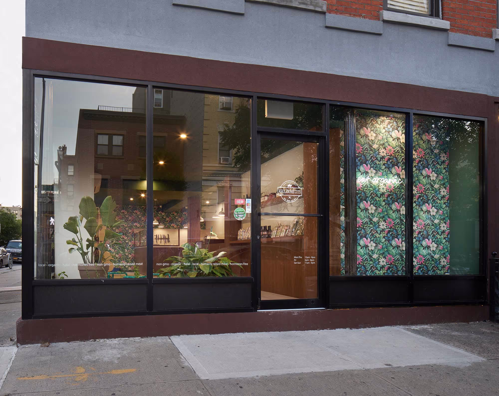 Contemporary storefront design of Wholesome Cuts butcher shop in Brooklyn, featuring modern retail architecture, full-height glass windows, and floral branding.