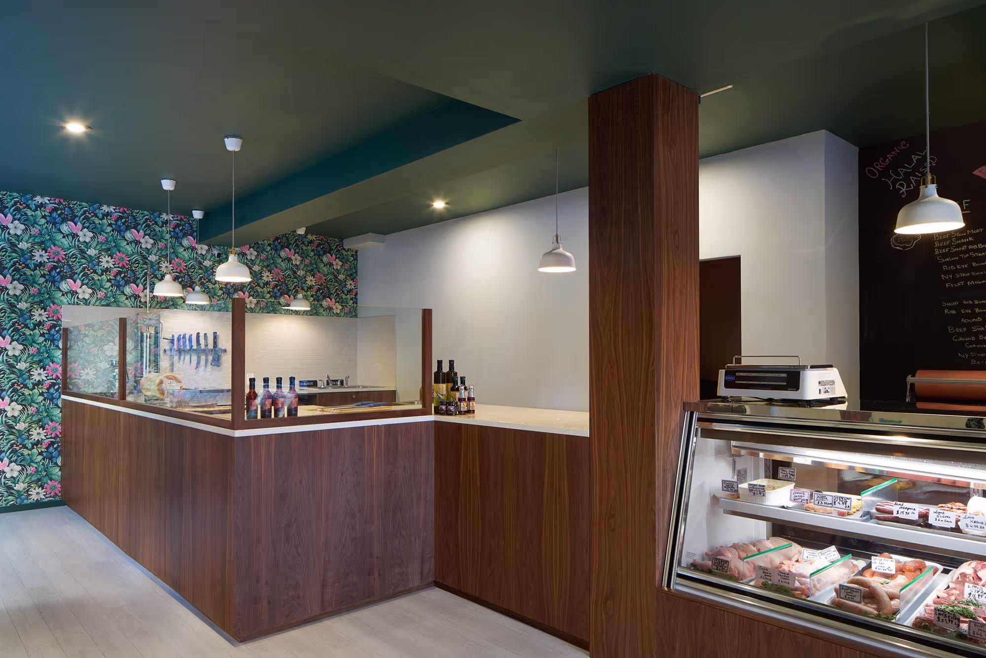 Modern butcher counter design at Wholesome Cuts in Brooklyn, combining floral accent walls, custom walnut cabinetry, and integrated lighting in a contemporary retail space.