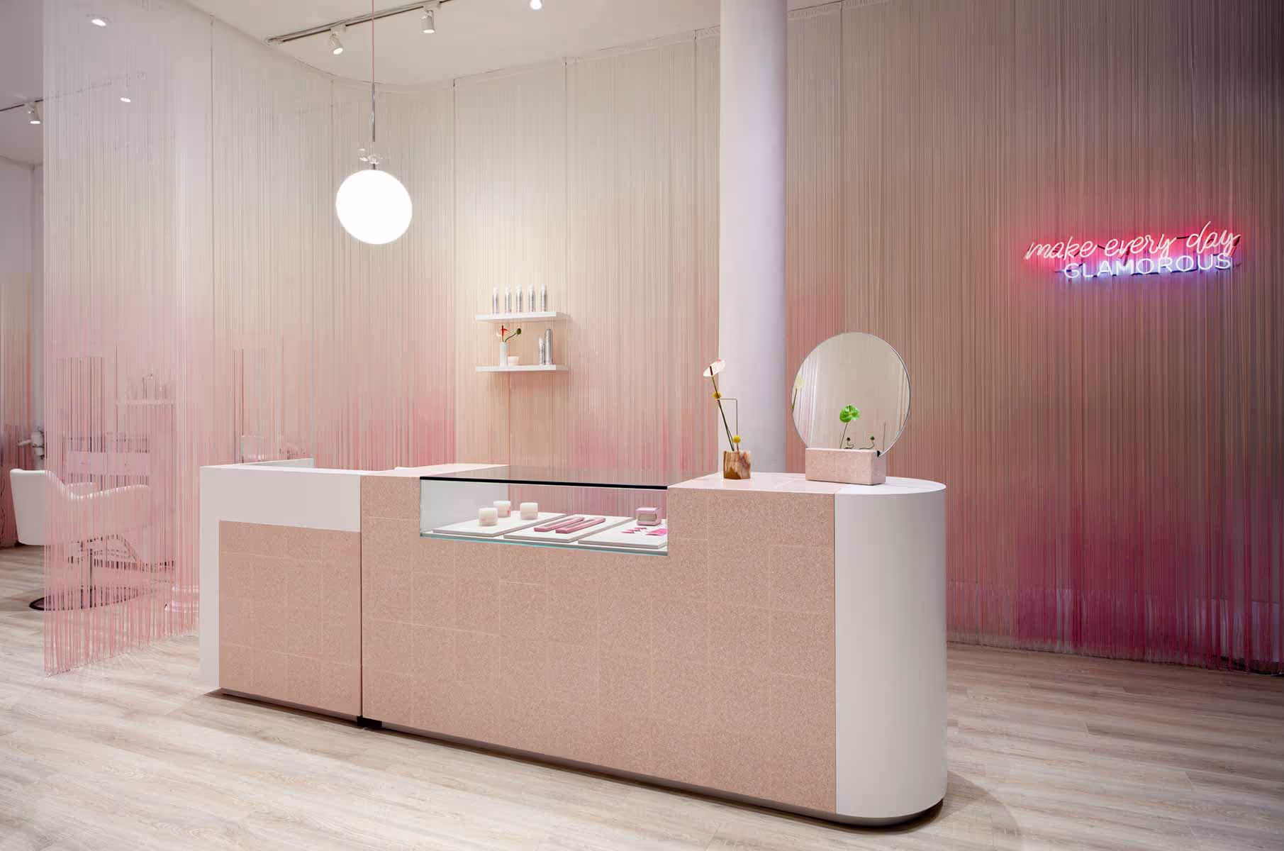 View of soft pink reception counter with round mirror and tiled counter detail. Feminine hair salon interior with modern beauty retail design.