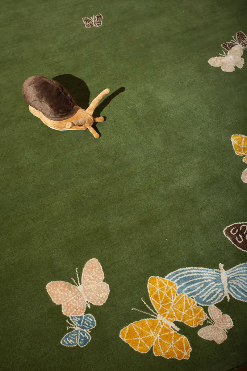 Zoomed-in view of the green rug surface with stuffed animal. Soft tonal variations and intricate butterfly wings.