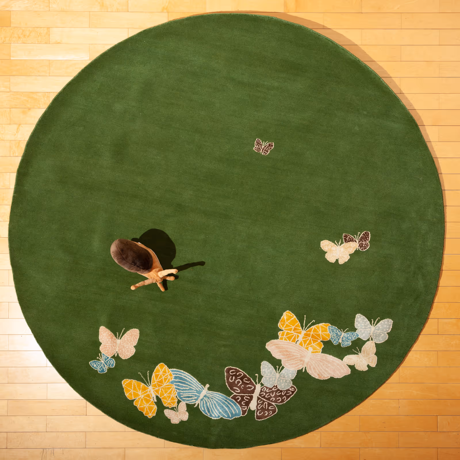 Top view of a green hand-knotted luxury rug with silk butterflies in yellow, pale pink, light blue, and brown