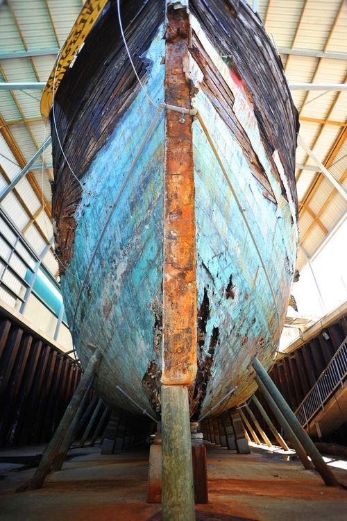 A weathered wooden boat with peeling blue paint, supported on wooden stilts inside a covered structure.