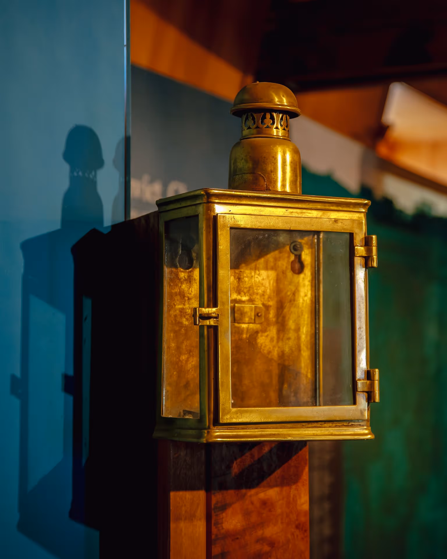 A vintage brass lantern with glass panels casts intricate shadows against a colorful backdrop.