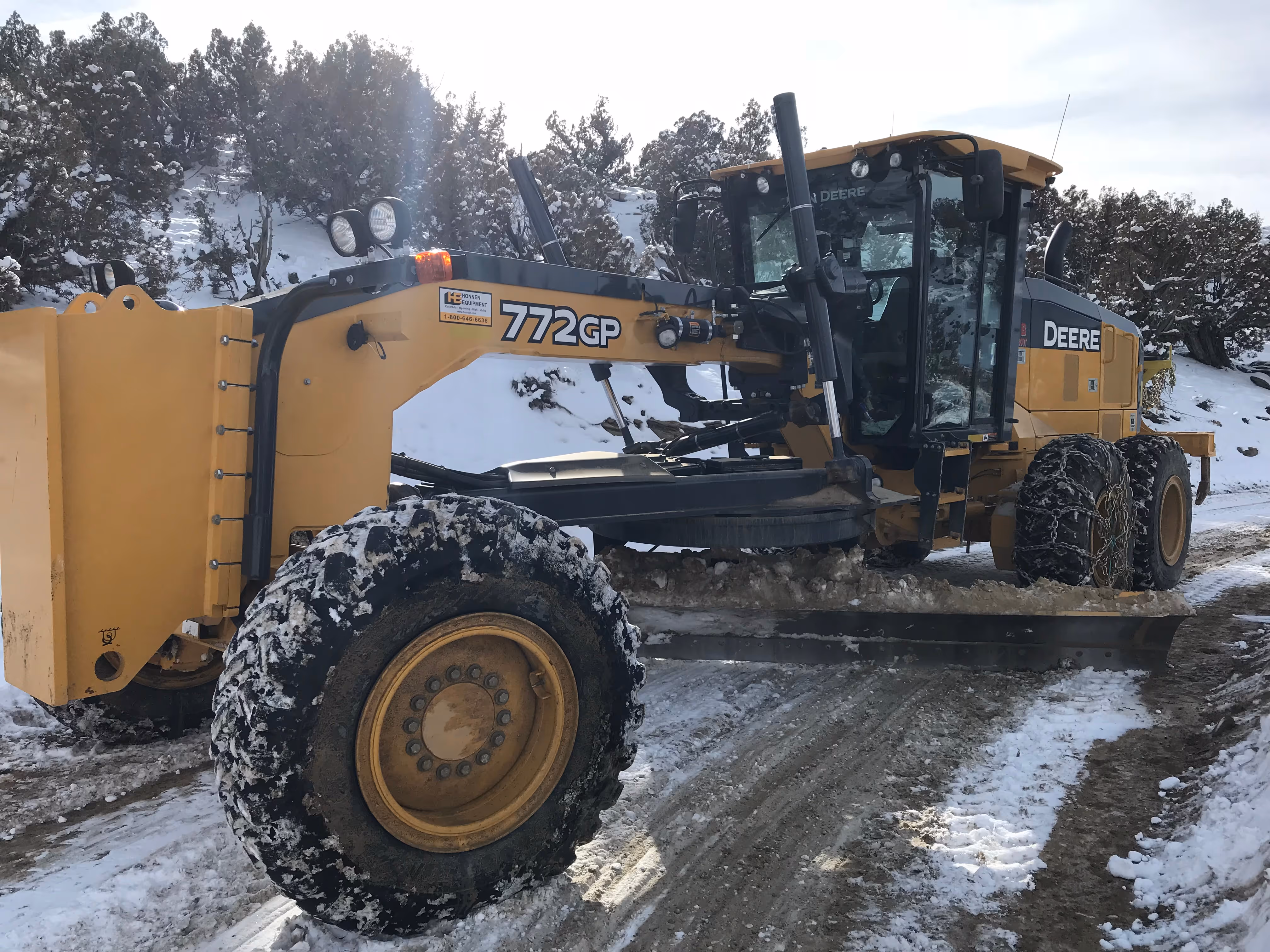 John Deere 772GP motor grader clearing snowy access road – B&B Roustabout Inc. providing reliable oilfield support and winter road maintenance services | www.bbroust.com