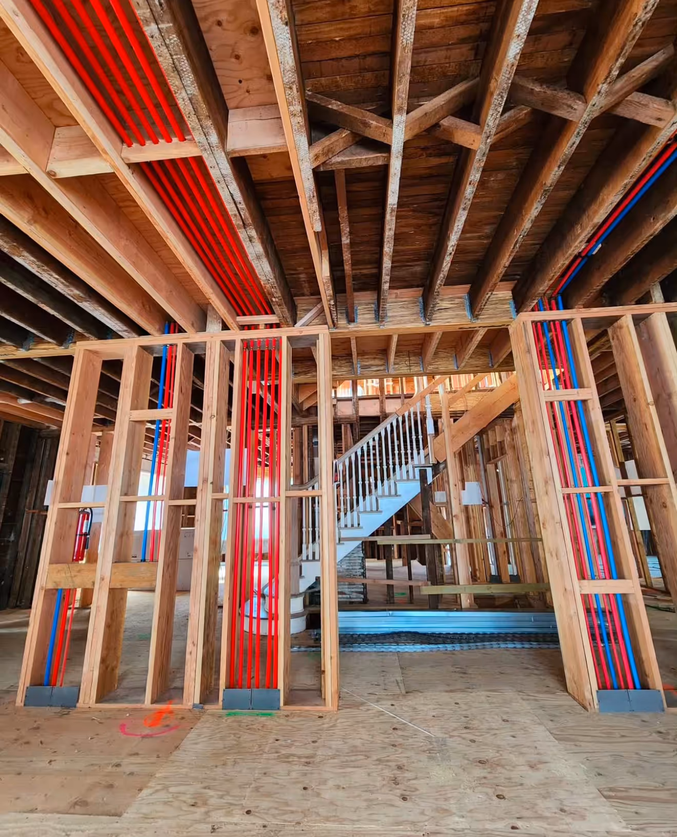 Framing stage of a home showing red and blue PEX plumbing lines neatly installed between wall studs and ceiling joints. 