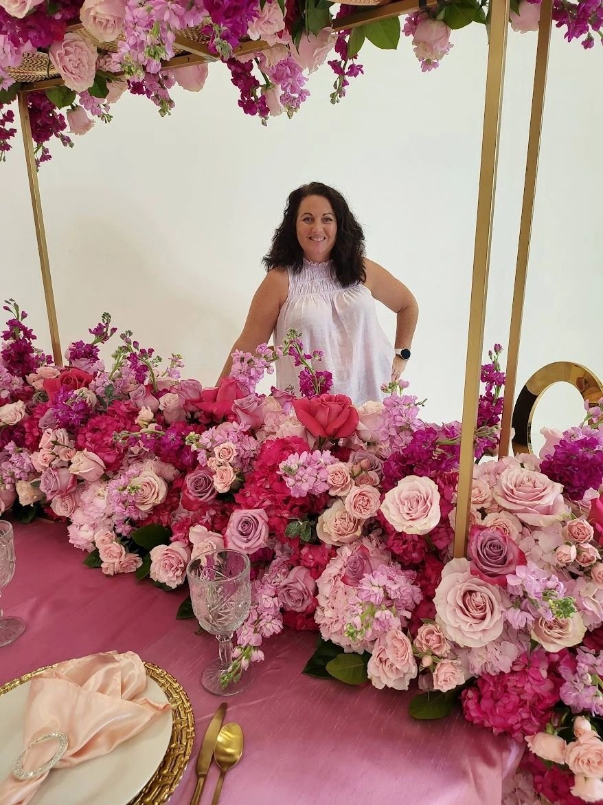Owner standing behind a pink and purple head table with flower decoration.