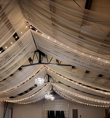 Linear ceiling draping with bistro lighting and chandeliers at Erie County Fair Grounds. 