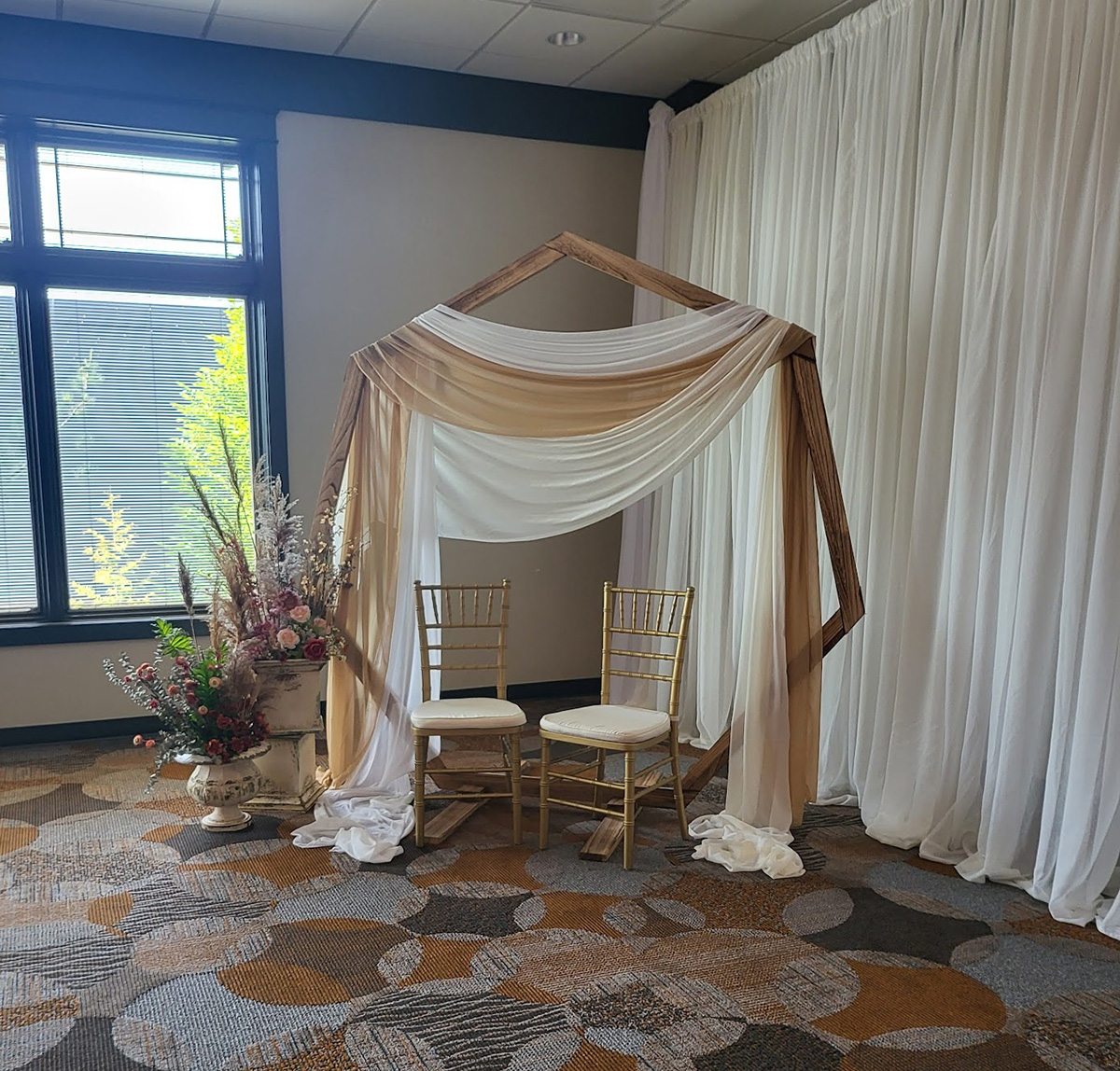 Seven-sided arch with white and gold fabric, chiavari chairs, and floral decorations. 