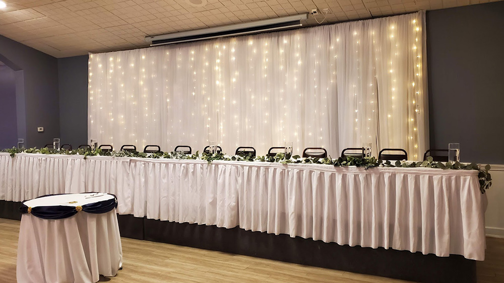 White table skirting on head table with a white fairy light backdrop. 