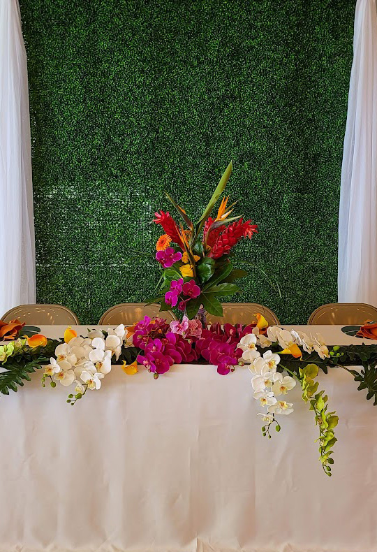 Tropical flowers on head table with green wall as backdrop. 