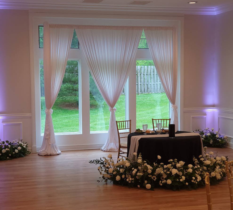 White fabric draping a floor to ceiling window behind the head table.